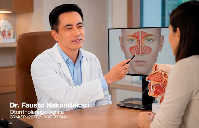 O médico ao lado de um monitor ou modelo anatômico, explicando a um paciente onde ficam os seios paranasais e por que o bloqueio da drenagem pode causar dor e pressão.